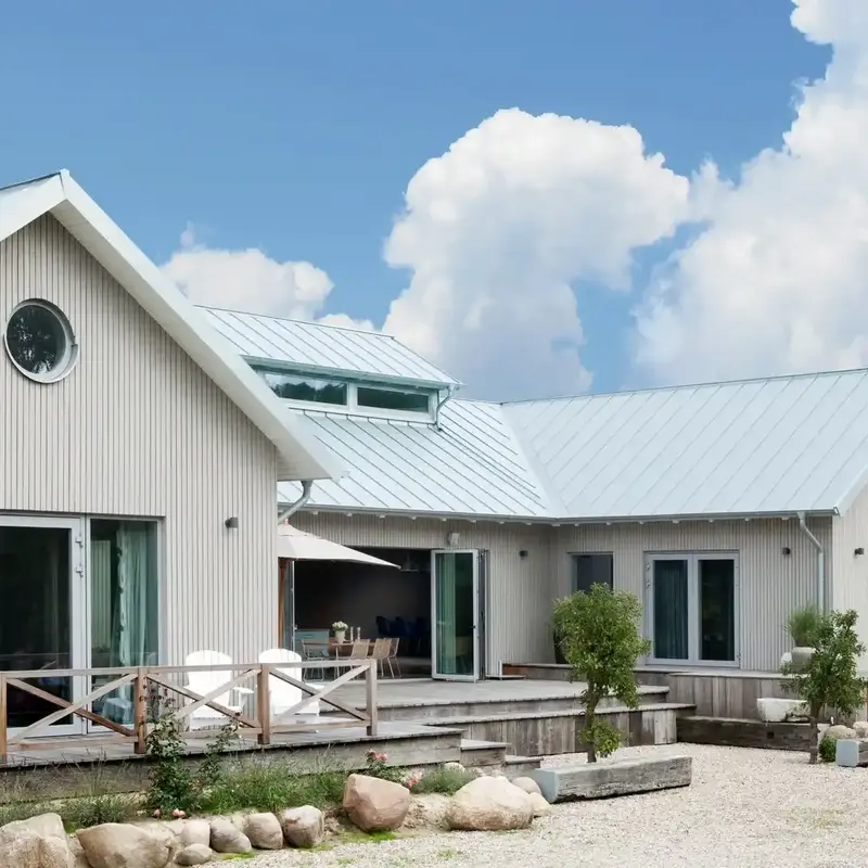 Haus im Landhausstil mit vertikaler Holzfassade in hellem Naturton sowie einem Metall Steildach und großzügiger Holzterrasse