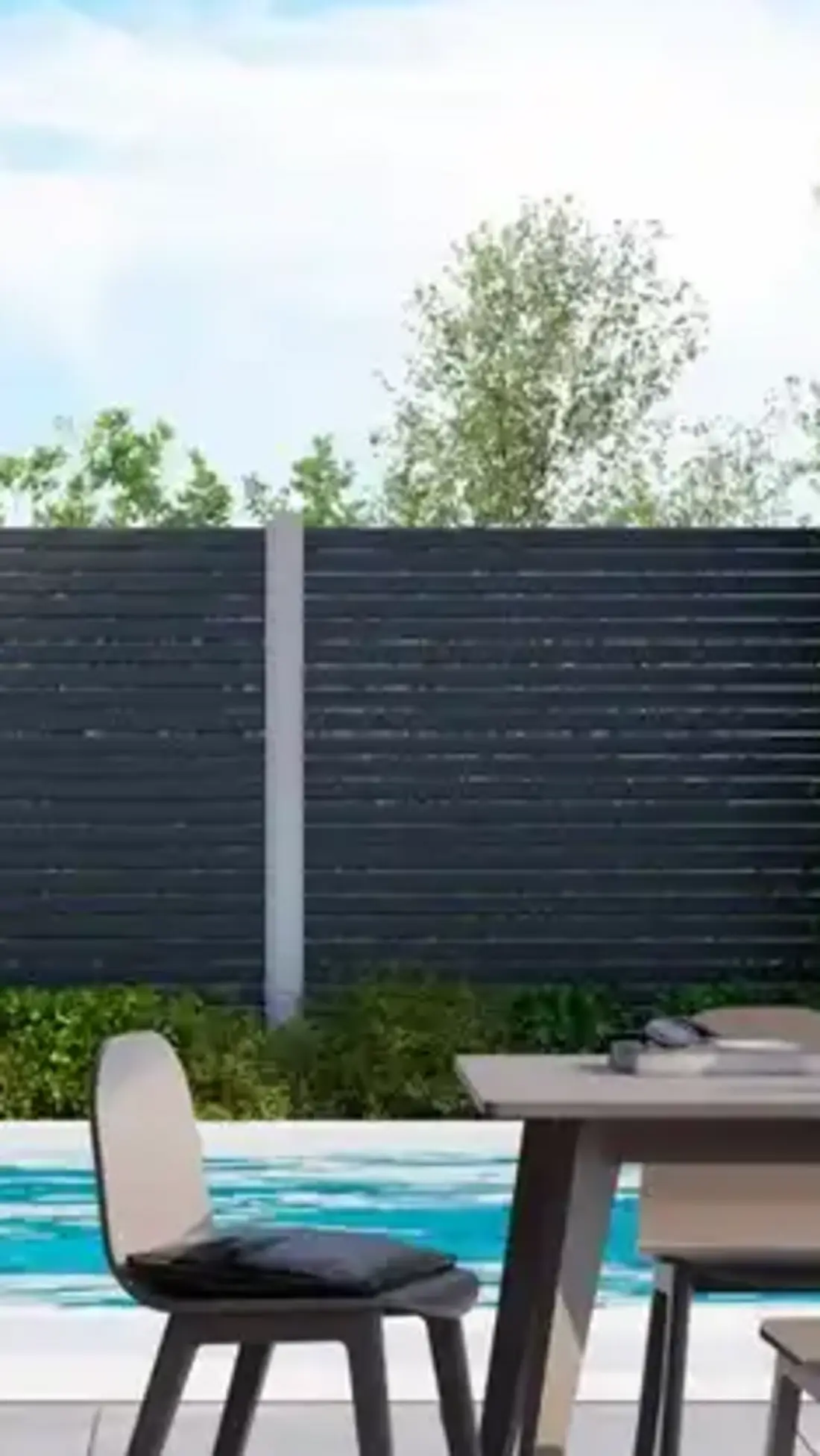 Blick über einen dunklen Sichtschutzzaun auf einen Pool mit Terrasse und Essbereich.