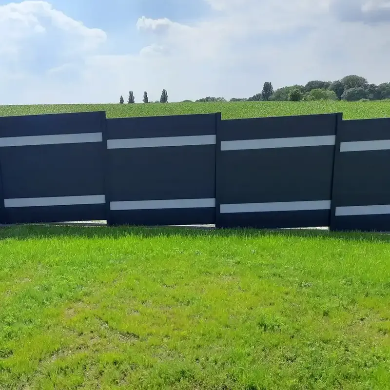 Dunkelgrauer Sichtschutzzaun mit zwei hellen Zierstreifen pro Feld auf einer grünen Wiese vor Feldlandschaft.